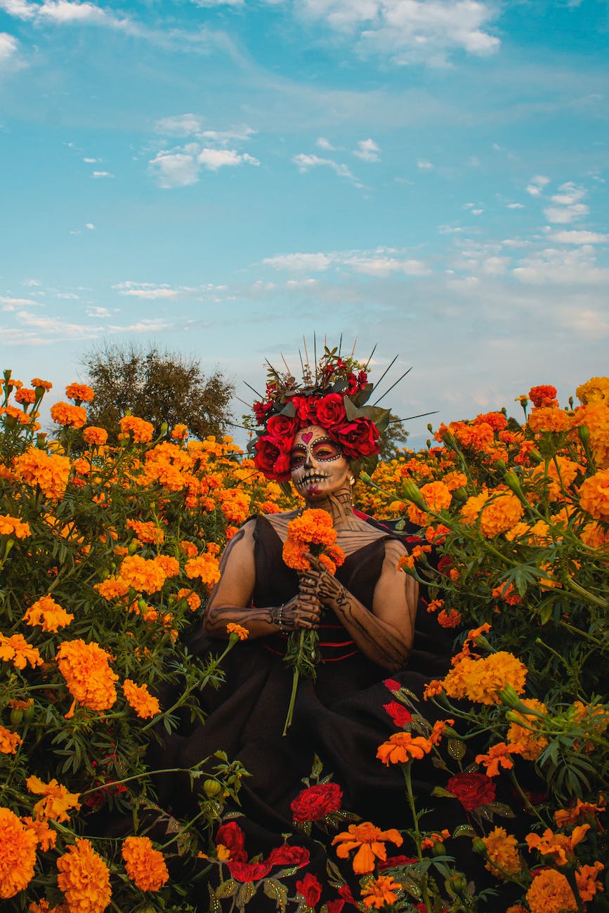 woman in makeup for the day of the dead in mexico standing on a field full of flowers